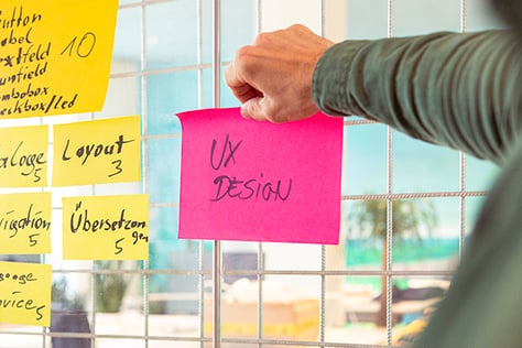 UX-Design in der Automatisierungstechnik: Eine Person fixiert ein Post-it mit „UX Design“ an ein Planungsboard, um benutzerfreundliche Softwarelösungen für den Maschinenbau zu entwickeln.